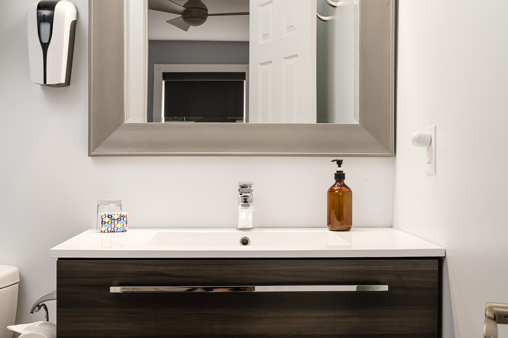 A bathroom vanity with white sink, large wooden framed mirror, and toilet.