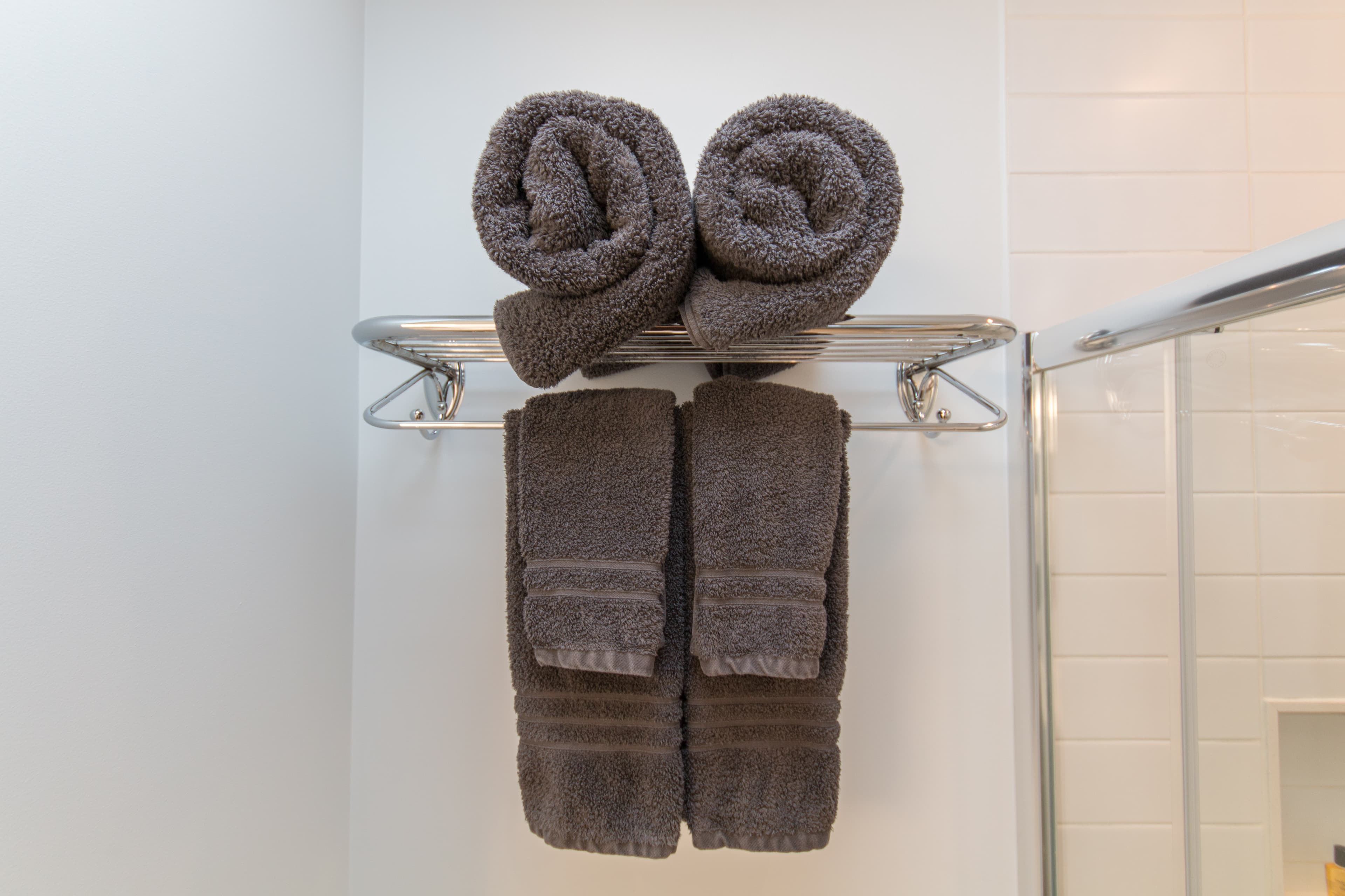 Clean, grey towels neatly folded and rolled on a rack in a bathroom.