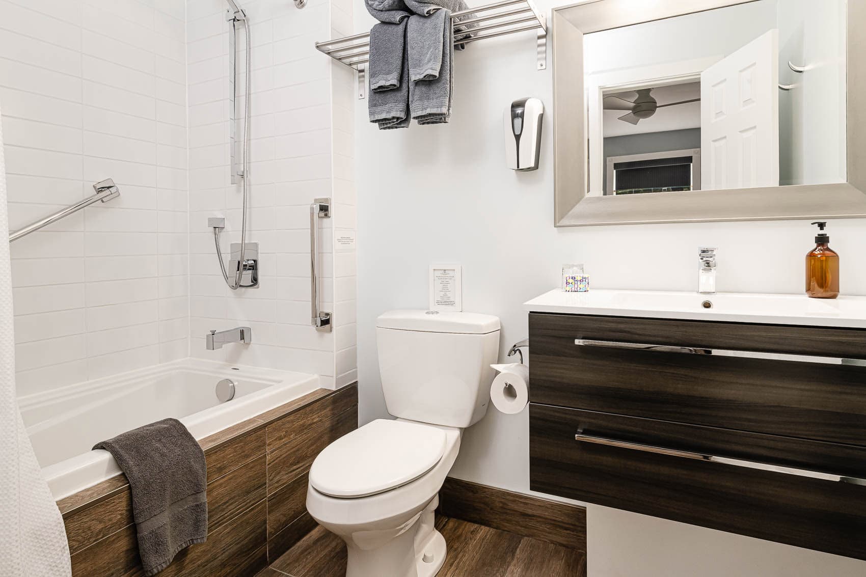 A clean bathroom with a combination soaking tub/shower, toilet, sink, mirror, and a shelf with towels.