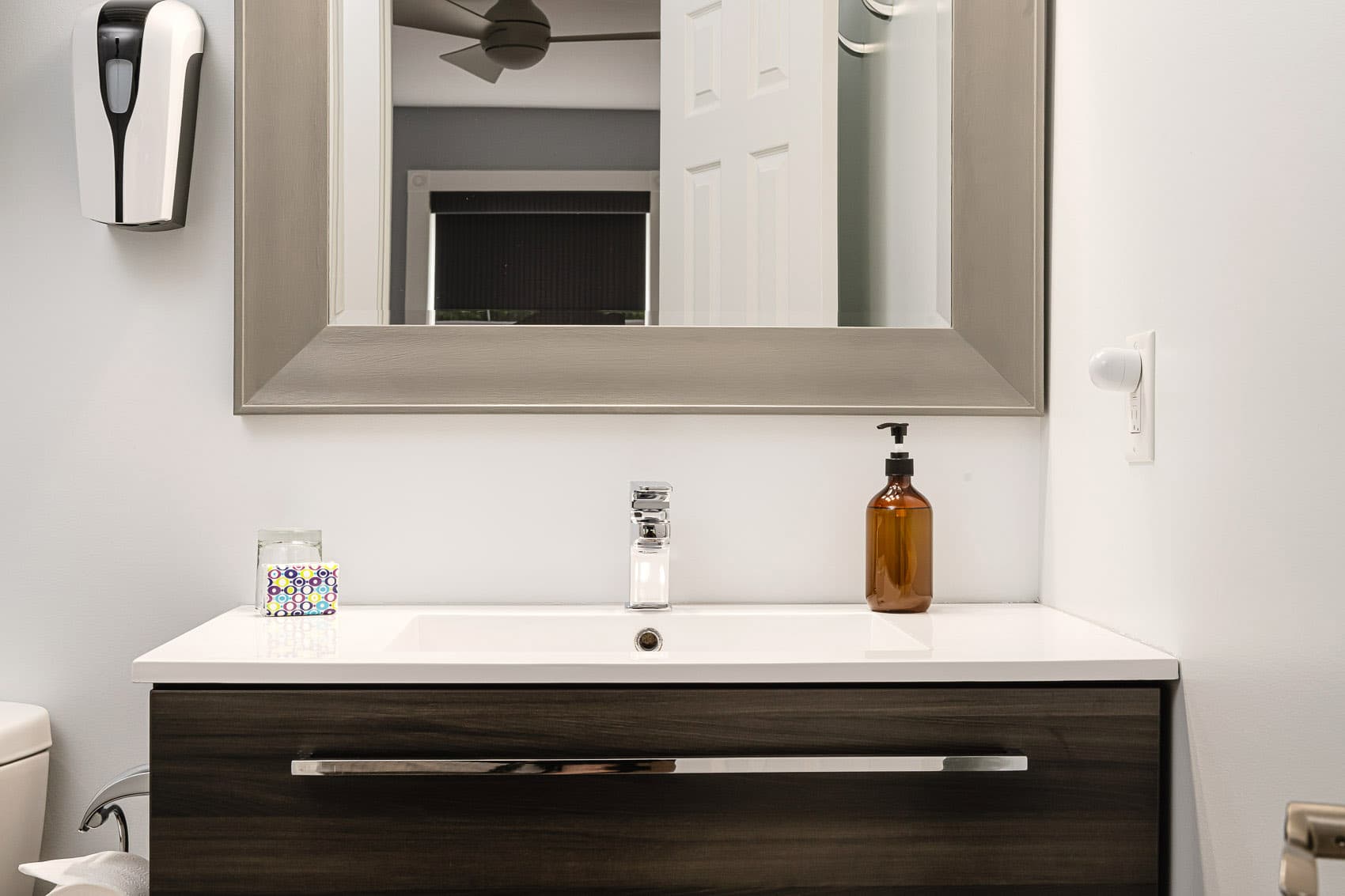 A bathroom vanity with white sink, large wooden framed mirror, and toilet.