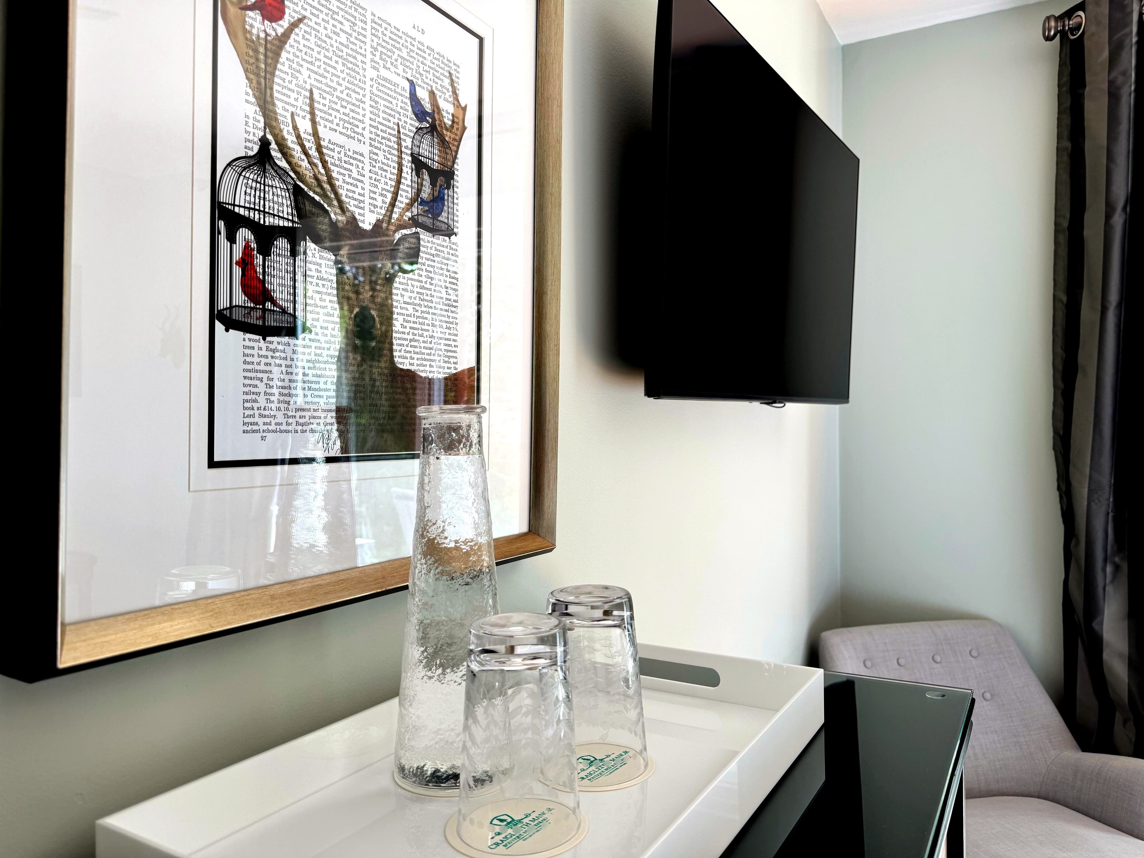 A tray with a glass water bottle and glasses on a dresser.