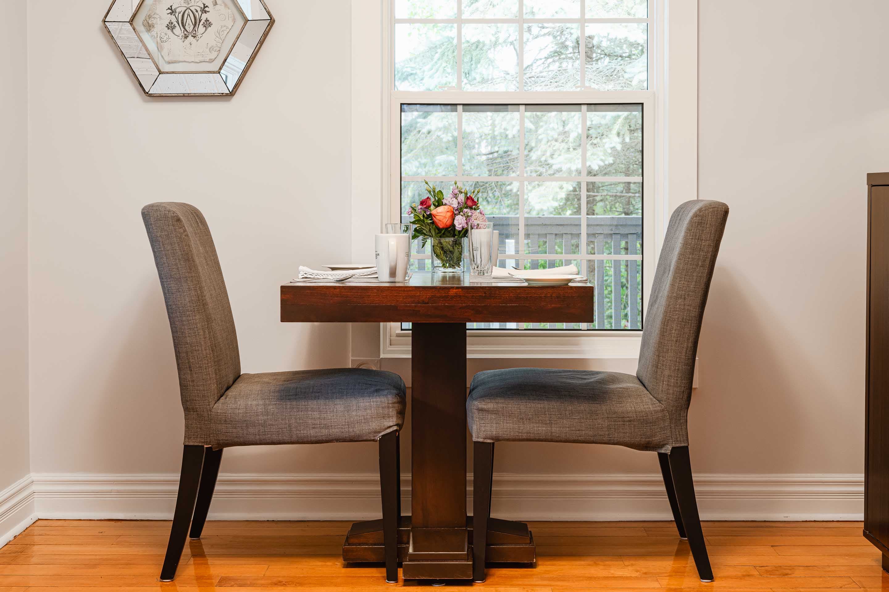 A cozy dining table set for two with a flower arrangement and natural light from a nearby window.