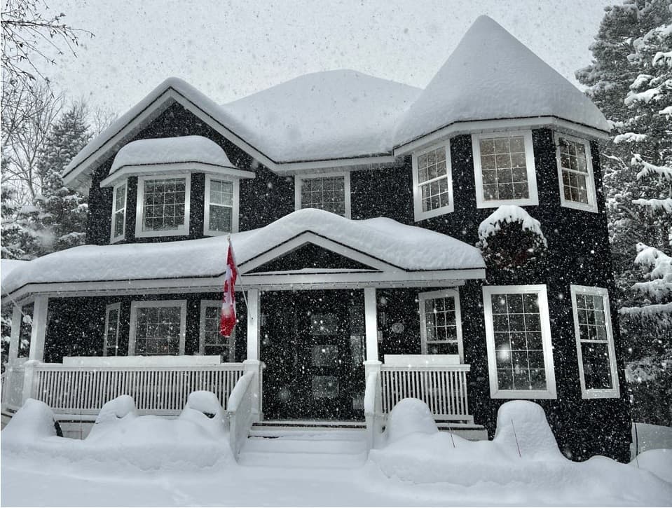 A large black house covered in snow with a Canadian flag, surrounded by falling snowflakes.