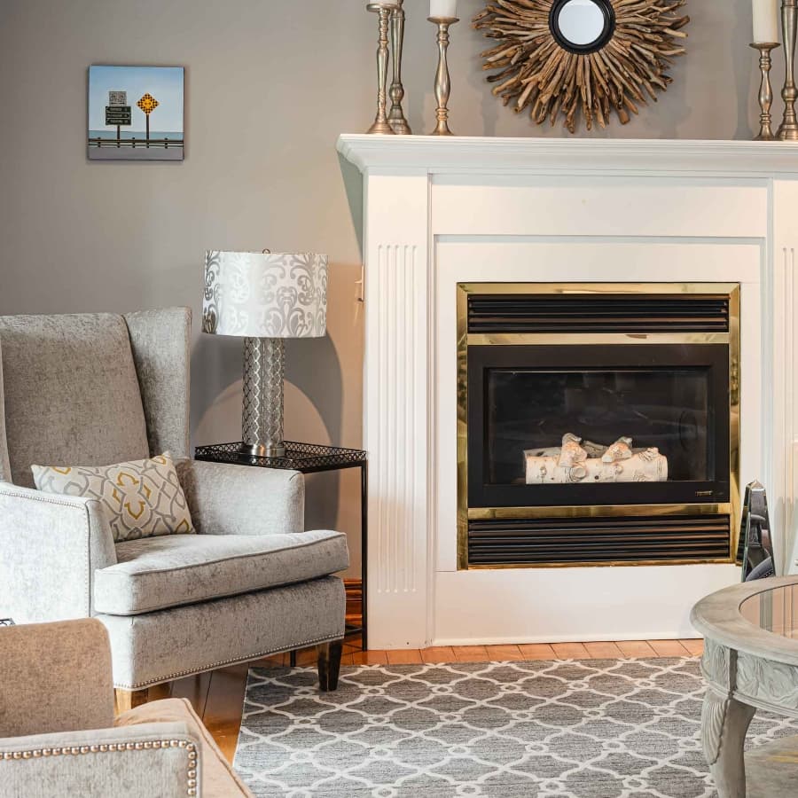 A cozy living room featuring a gray armchair, decorative lamp, and a modern fireplace.