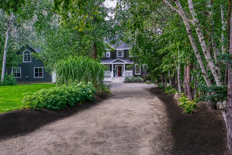 View of driveway into manor house with green grass and tree lined