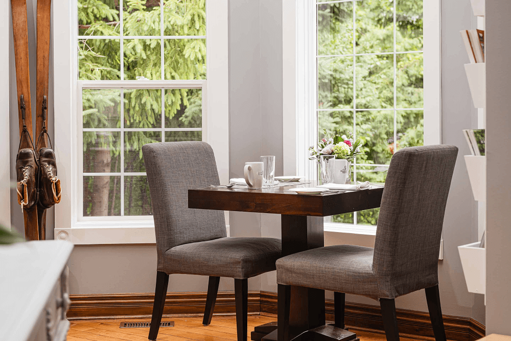 Cozy dining nook with two chairs, a small table, and large windows overlooking greenery.