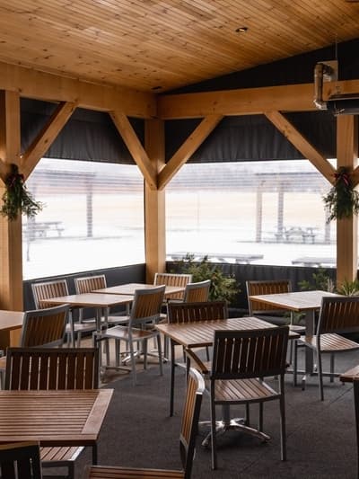 A cozy wooden interior with empty tables and chairs under a shelter.