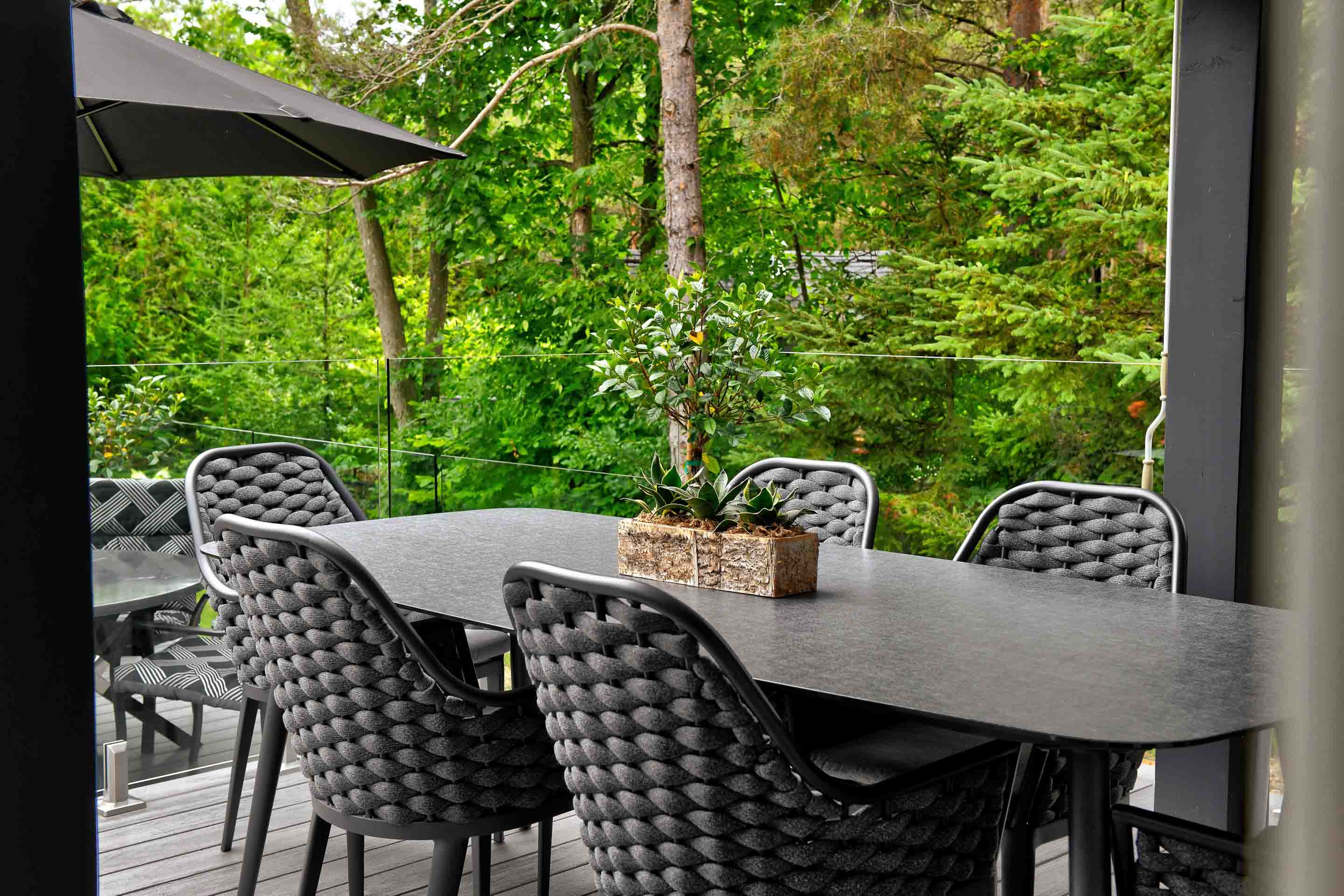 A stylish outdoor dining area with a dark table, woven chairs, and lush greenery in the background.