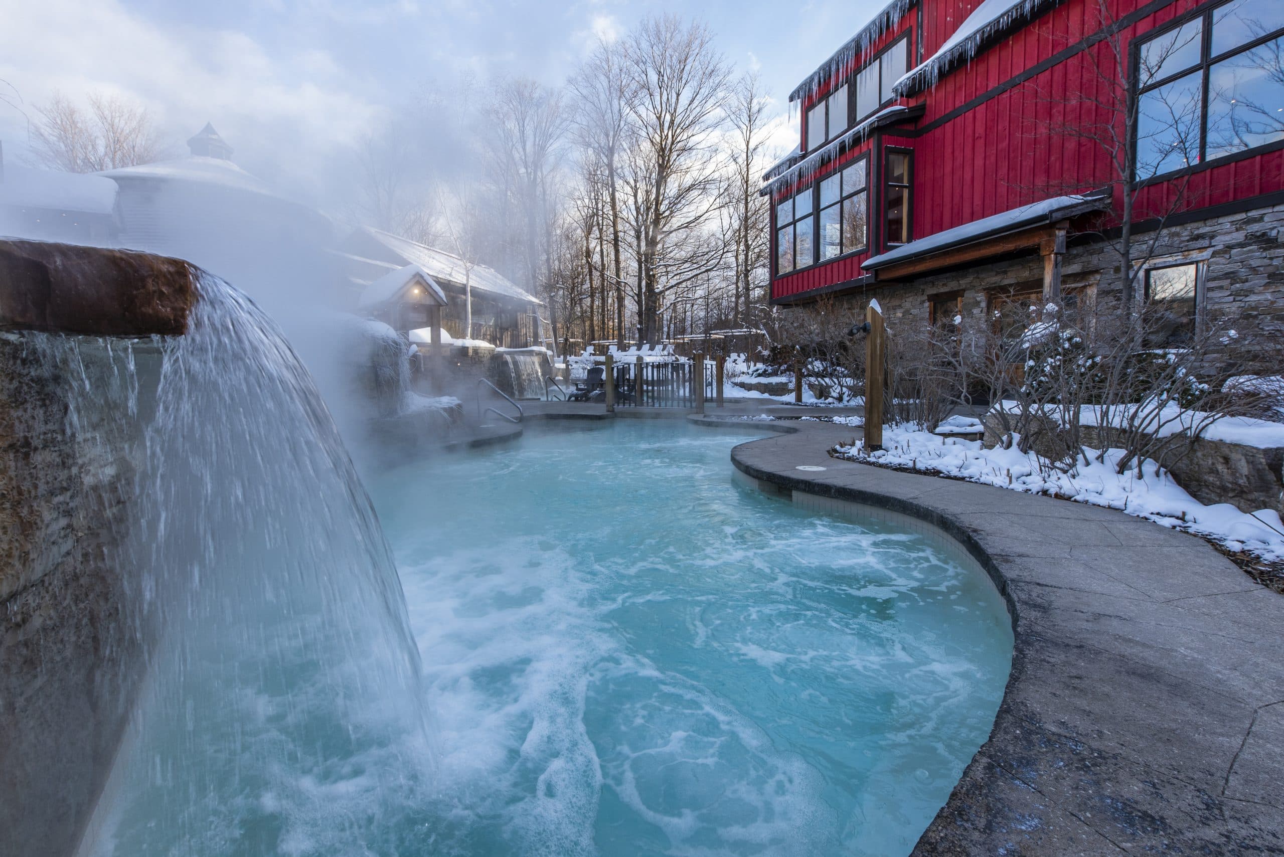 A steaming hot spring pool surrounded by snowy trees and a modern red building.