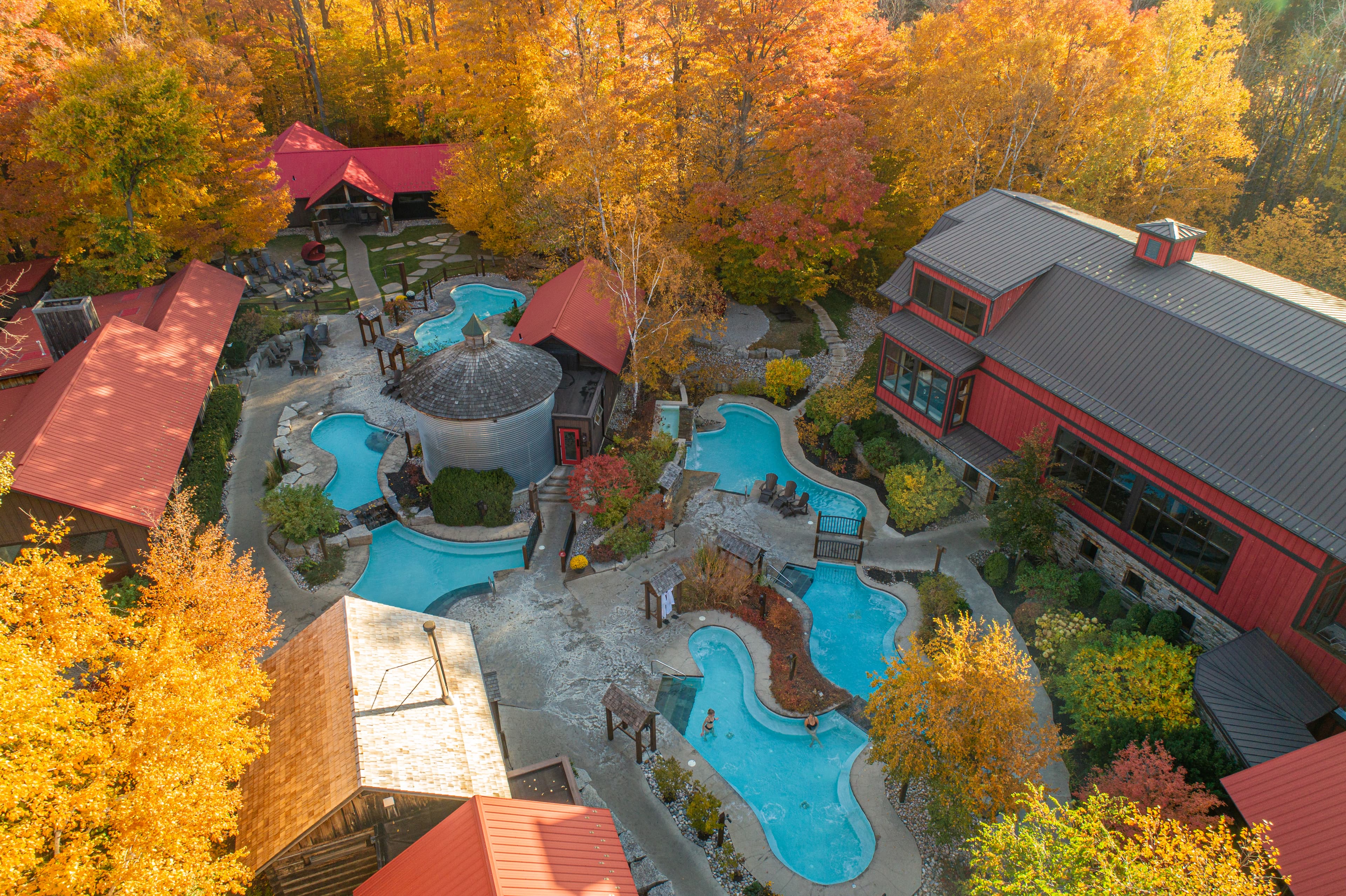Aerial view of a resort with pools surrounded by vibrant autumn foliage.