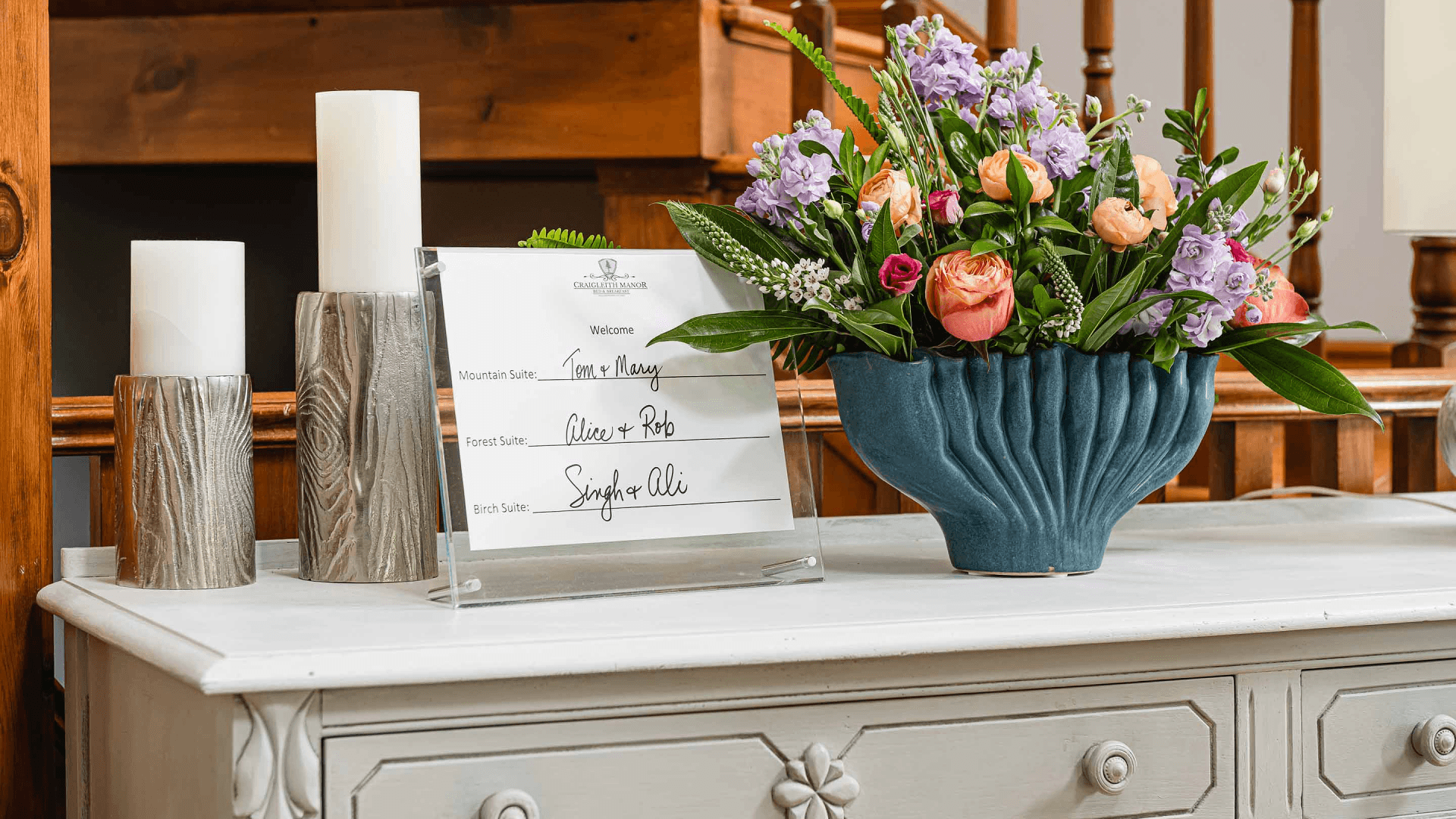 A welcoming display featuring a floral arrangement and a sign listing guest names on a white table.