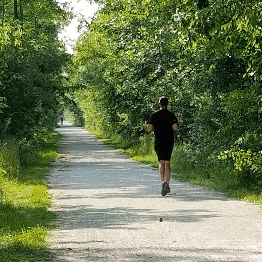 Man in black running clothes jogging on tree lined Georgian Trail