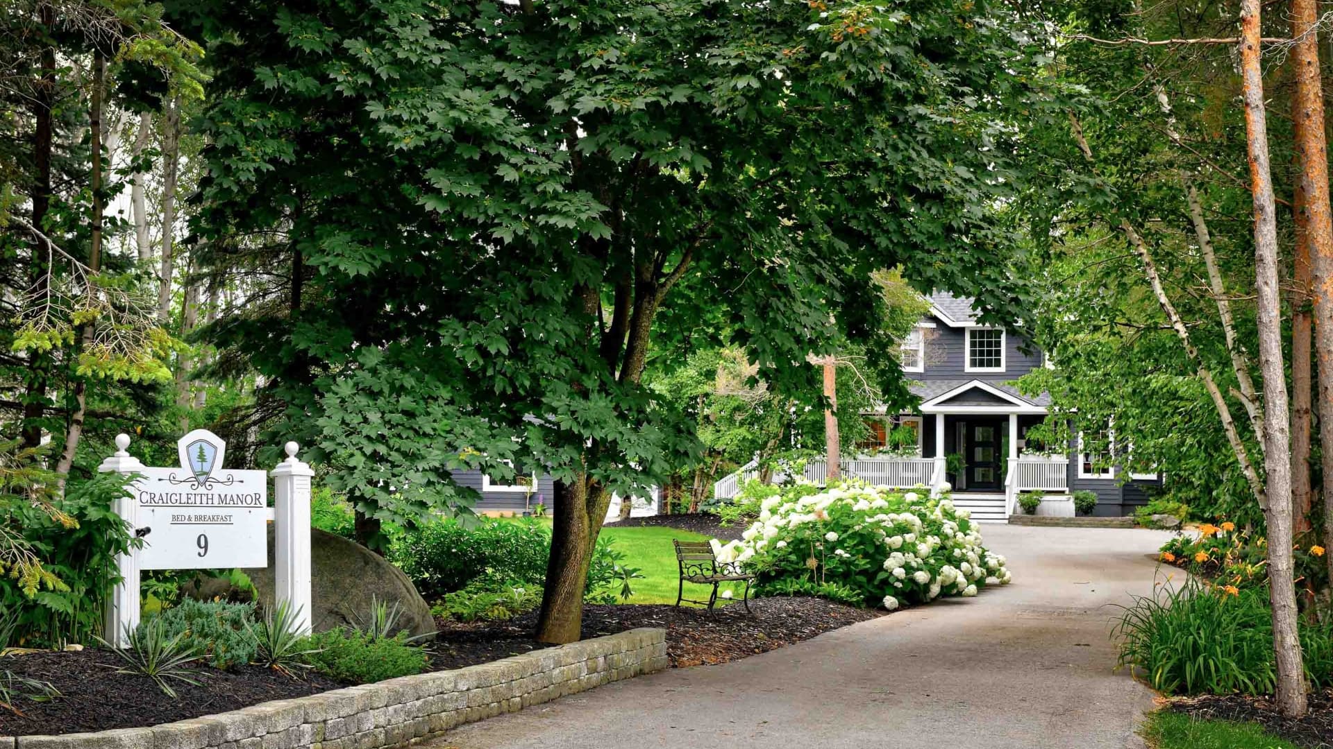 A picturesque bed and breakfast entrance framed by lush greenery and vibrant flowers.