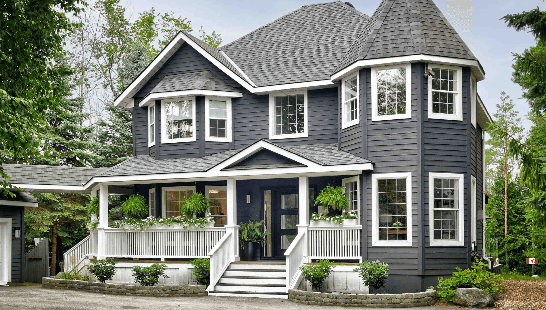 A two-story dark gray house with multiple windows and a front porch, surrounded by greenery.