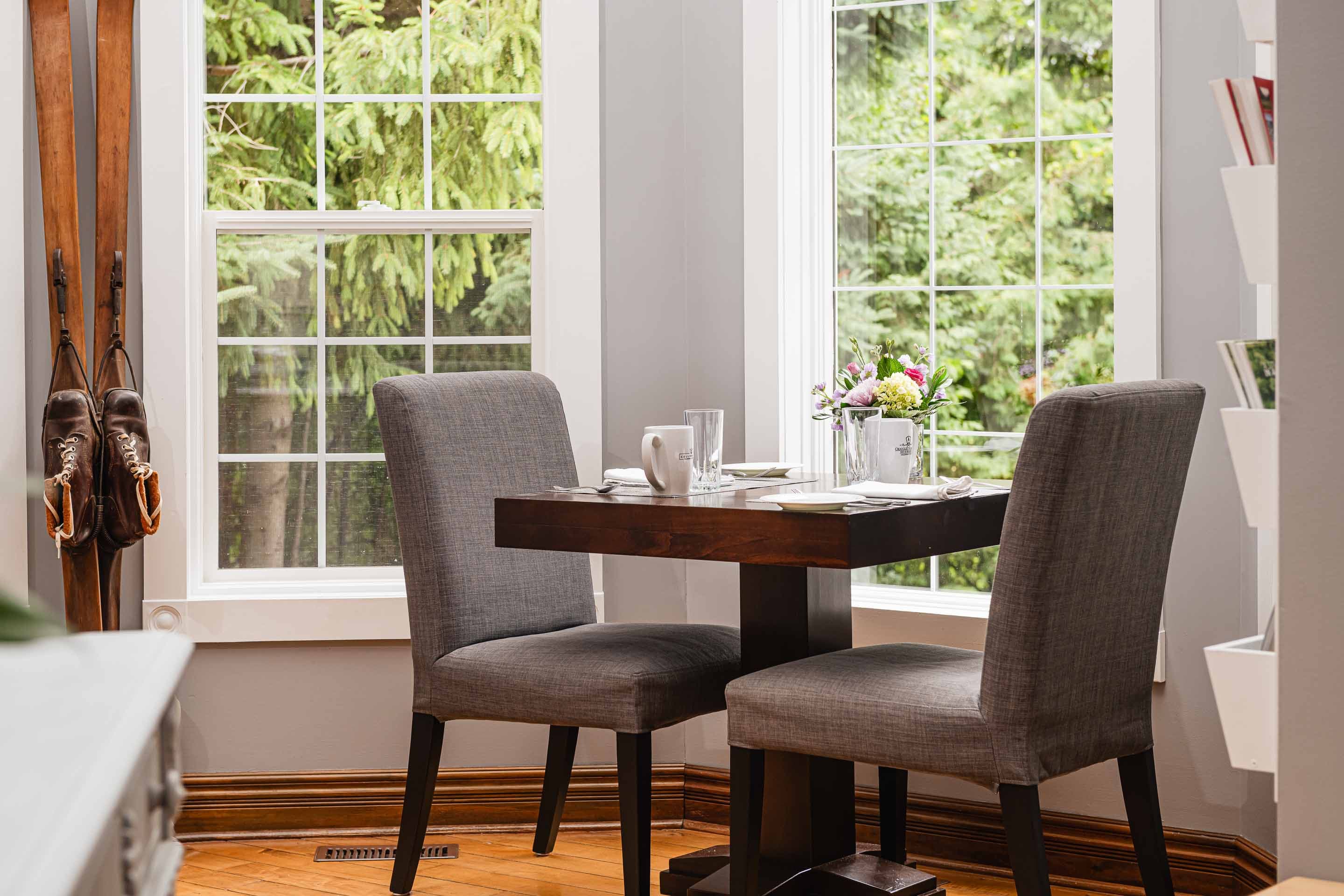 A cozy dining nook with two chairs and a table near large windows overlooking greenery.