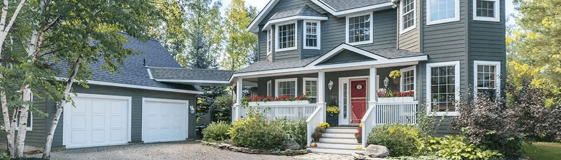 Front view of 2 story Craigleith Manor house and garage, gray siding, red front door and white trim, steps up to front door.