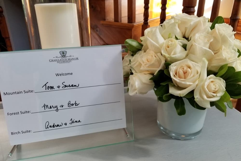 A welcome sign lists the names of guests beside a bouquet of white roses.