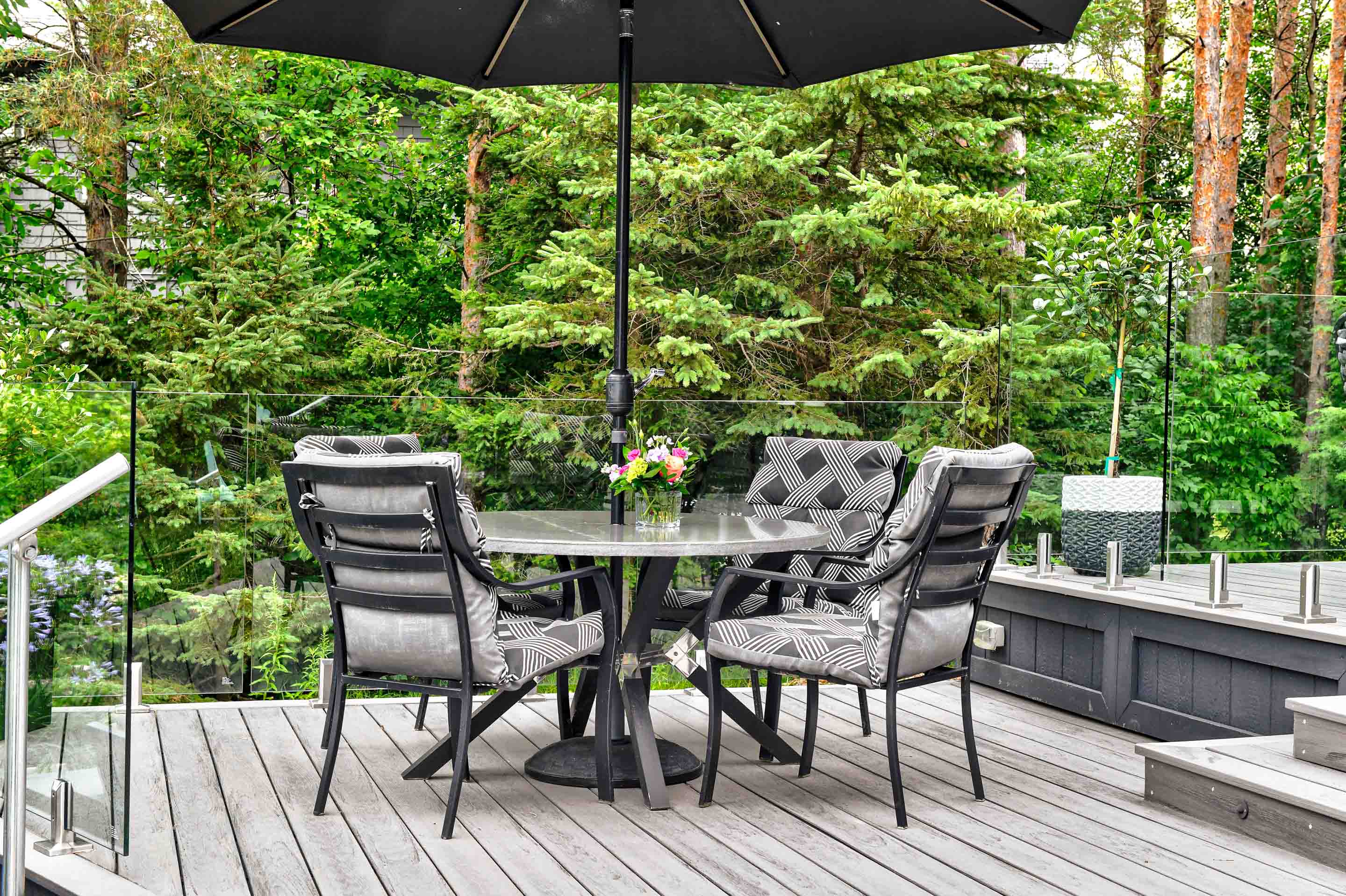 A patio dining area with a table, four chairs, and an umbrella, surrounded by lush greenery.