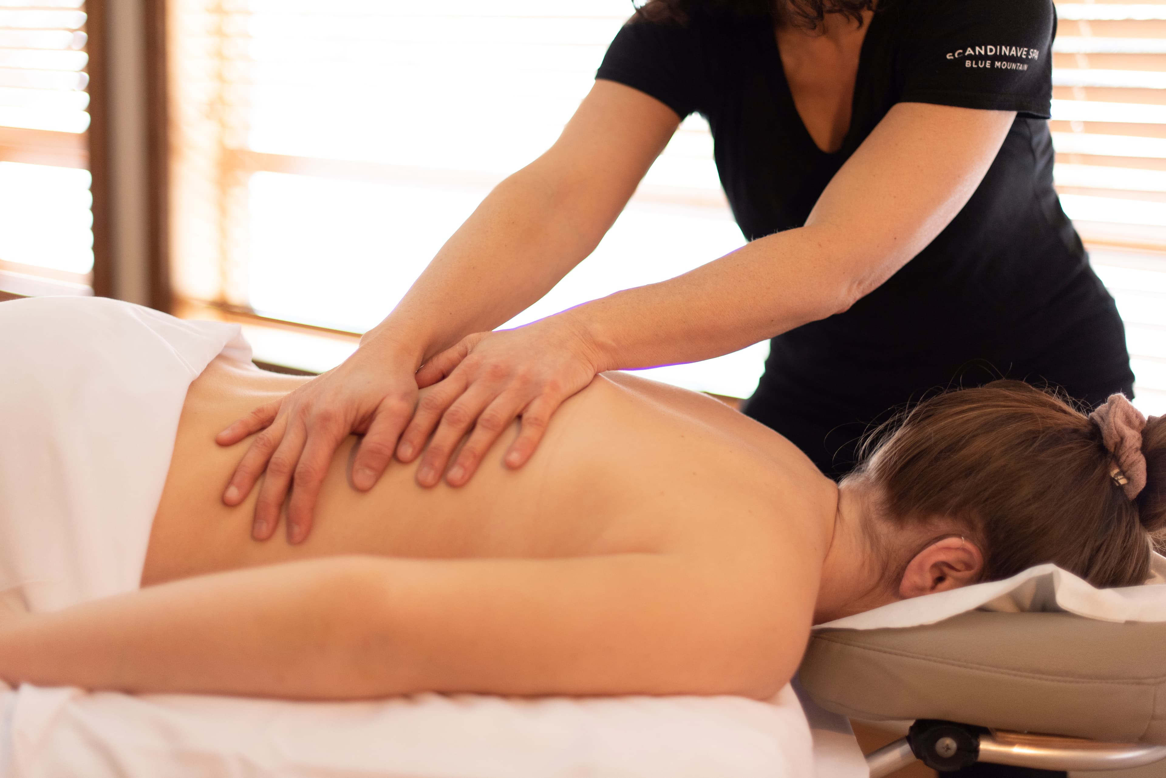 A massage therapist applies pressure on a client's back in a serene setting.