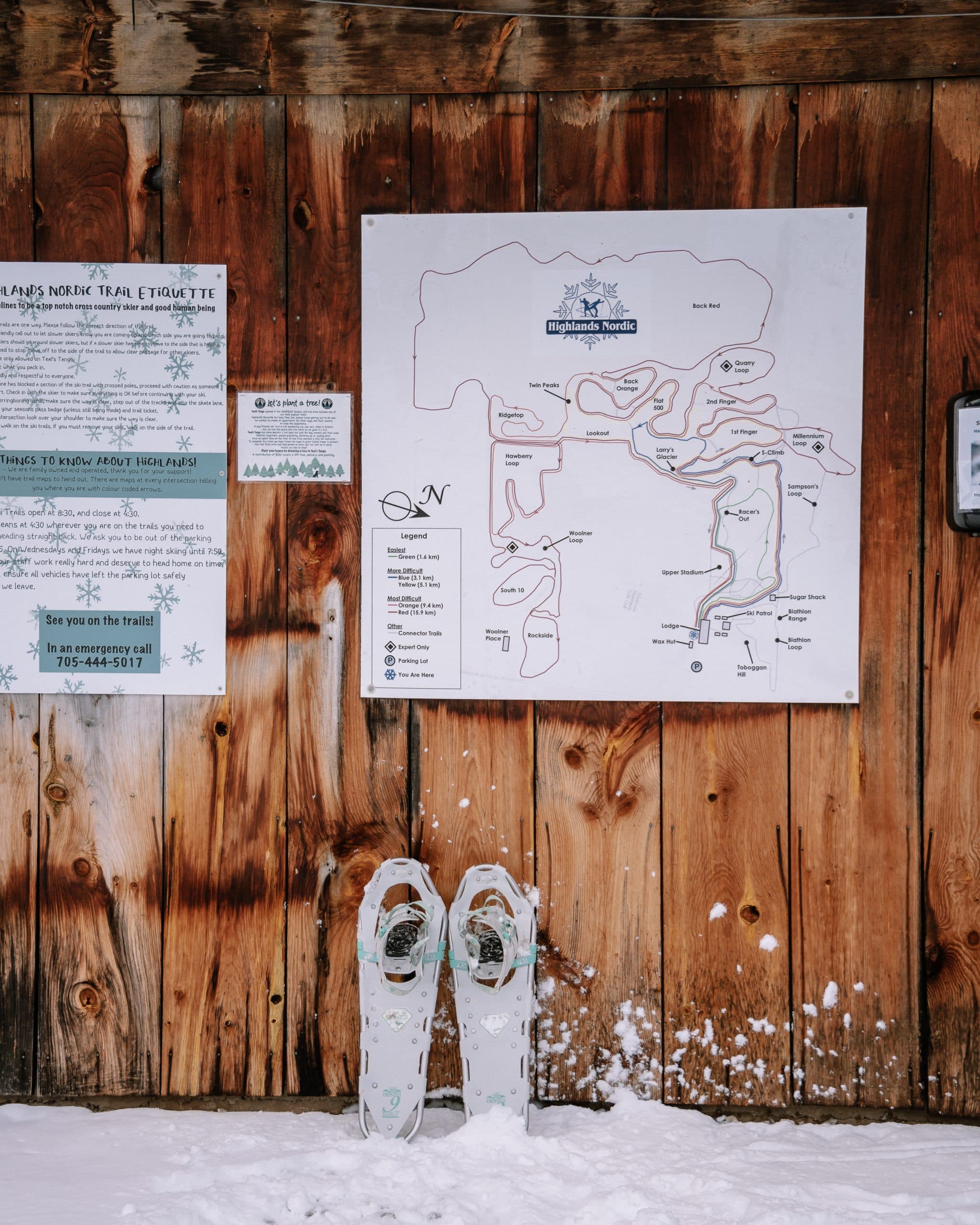 A snow-covered ground with a map of Highlands Nordic trails and a pair of snowshoes leaning against a wooden wall.