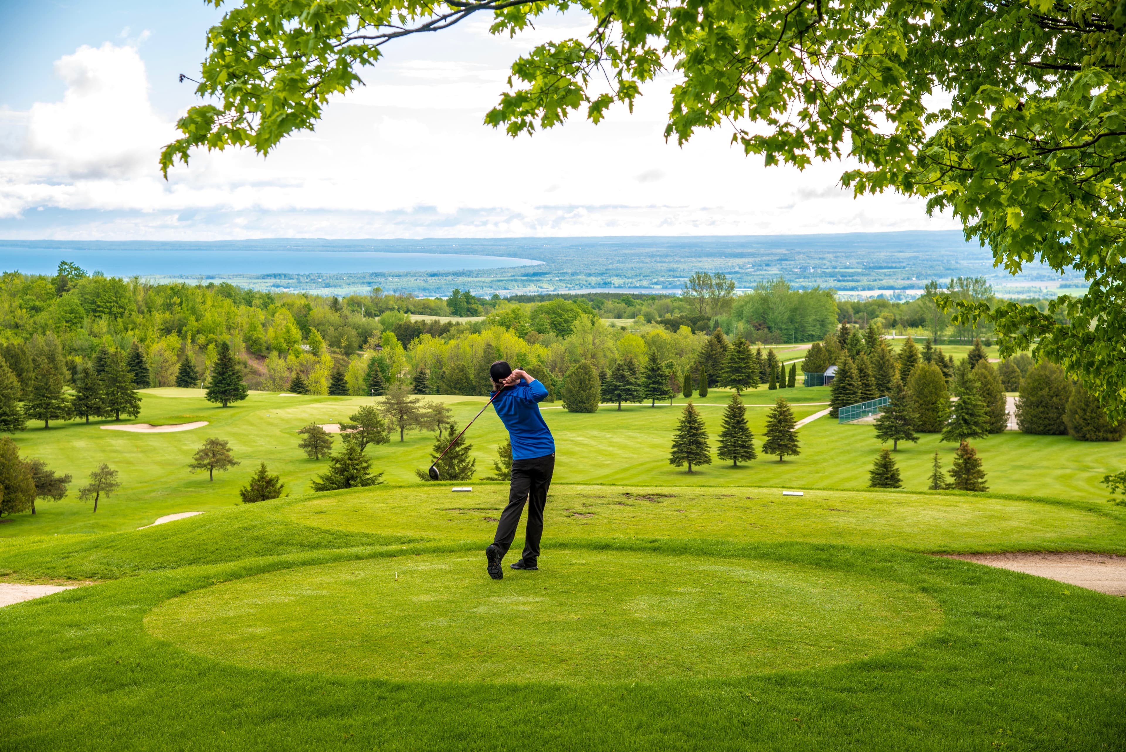 A golfer swings a club on a lush course overlooking a scenic landscape.