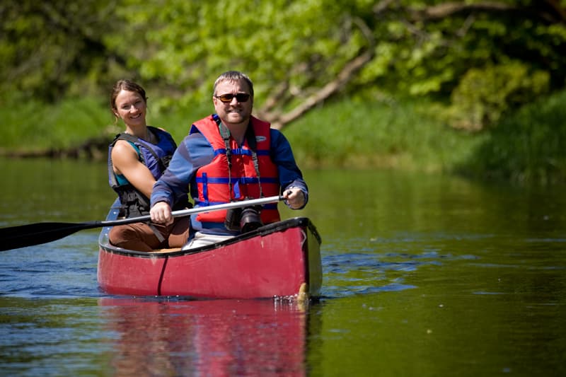 A man and woman paddle a red canoe on a calm, green river. A man and woman paddle a red canoe on a calm, green river.