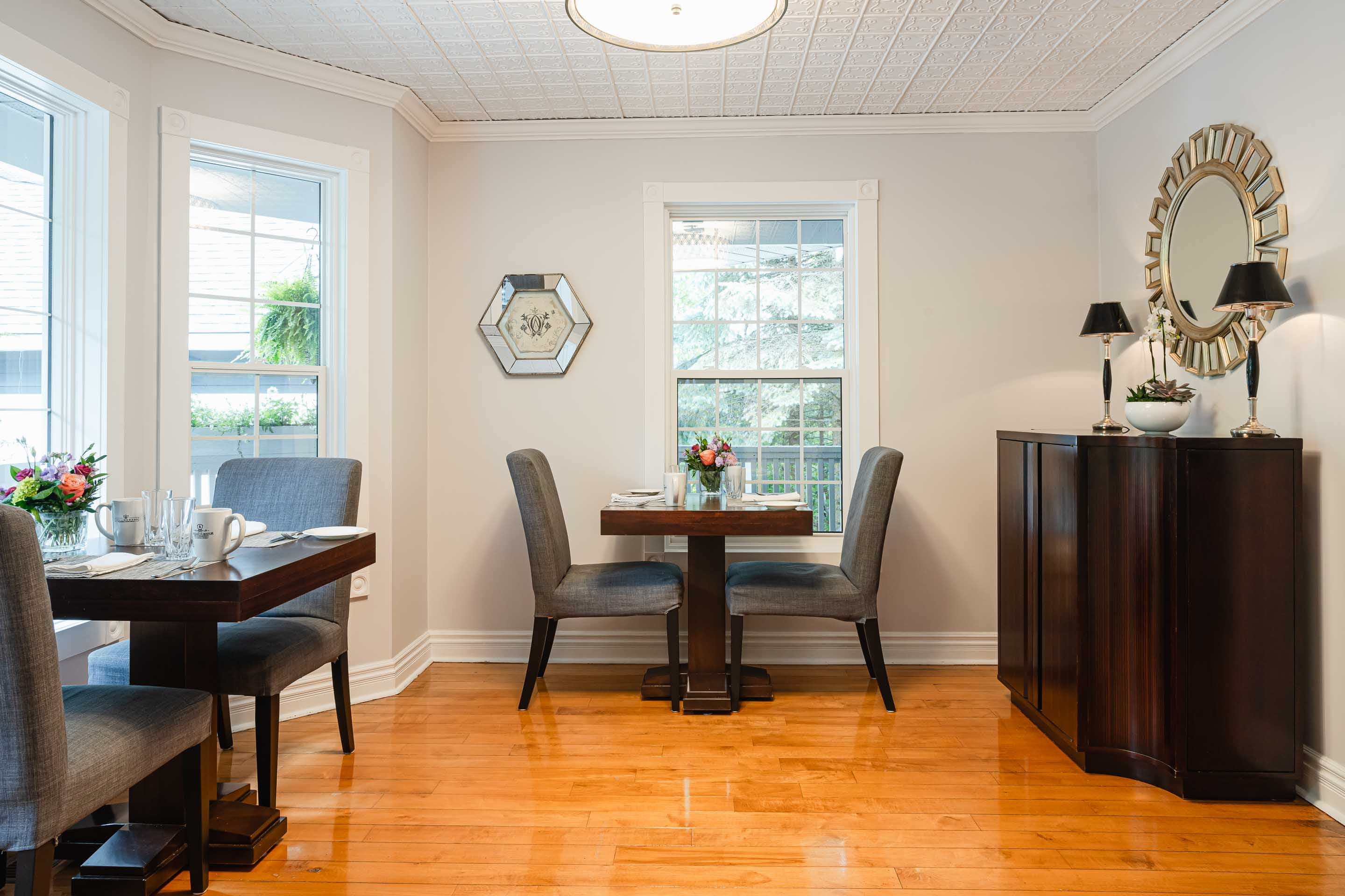 Bright dining area featuring two tables, modern decor, and natural light from large windows.
