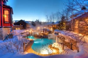 A picturesque winter scene featuring a steaming outdoor pool surrounded by snow-covered landscapes and cozy buildings.