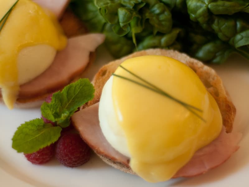 Eggs Benedict with ham on toasted English muffins, topped with hollandaise sauce, garnished with mint and raspberries.