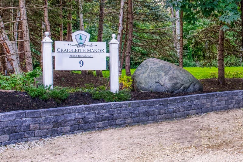 Craigleith manor white monument sign with trees and large boulder in front of rock wall