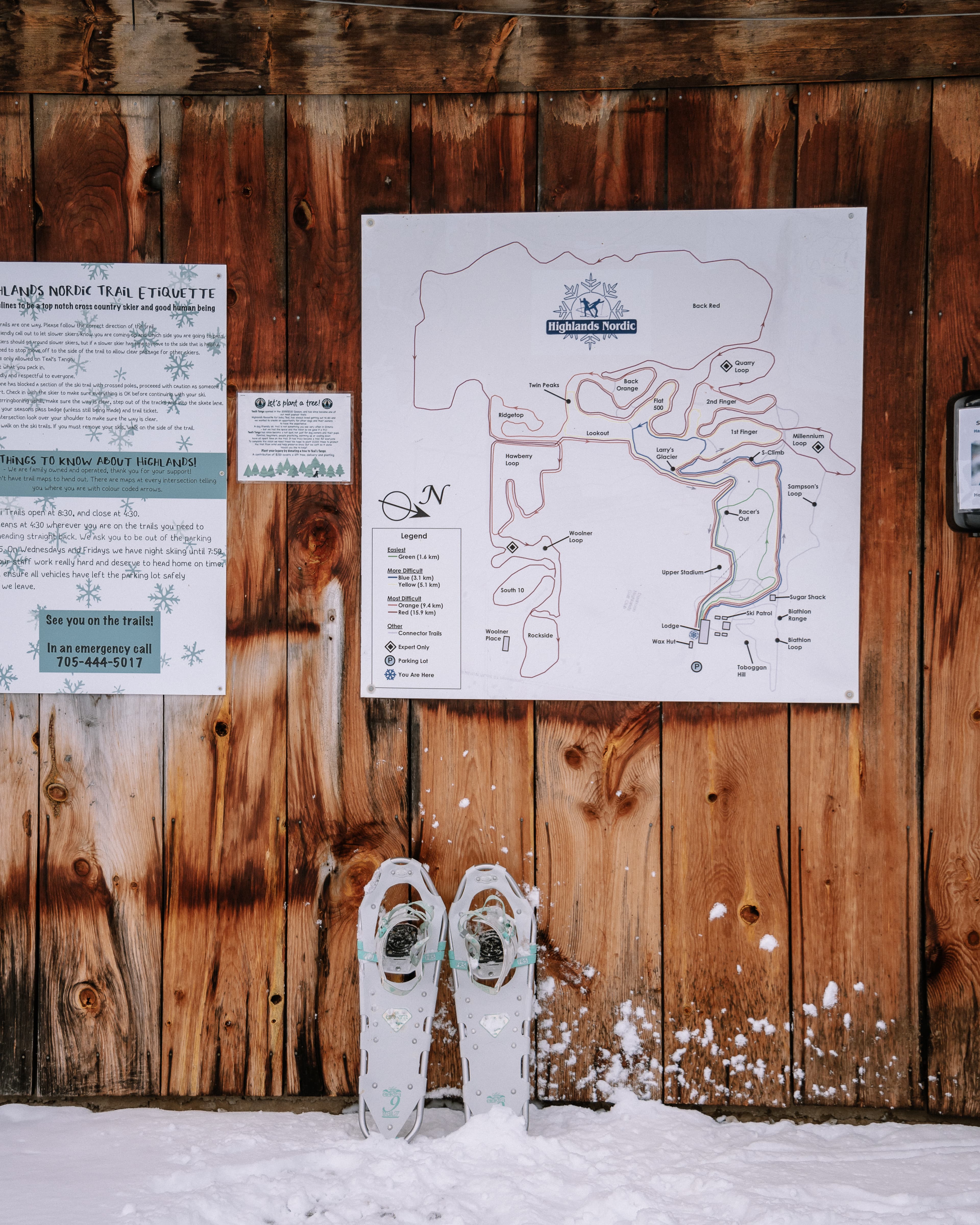A snowshoe stands against a wooden wall beside a trail map at the Highlands Nordic Center.