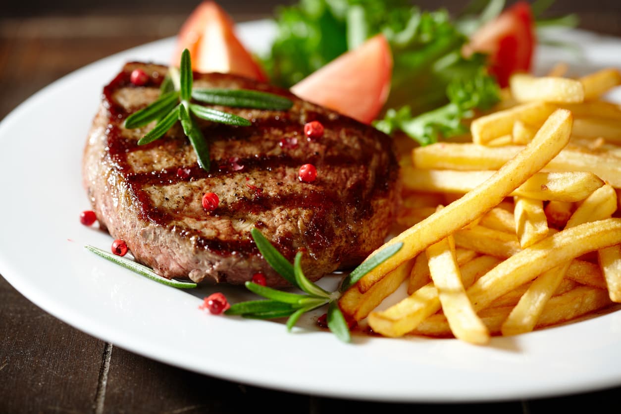 A grilled steak topped with rosemary, served with fries and fresh tomato slices.