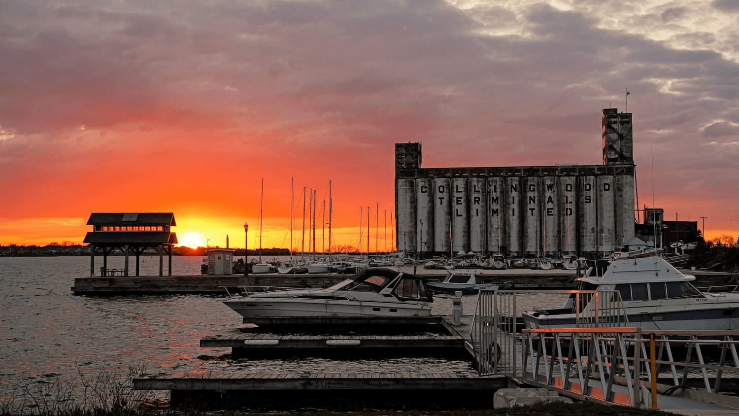 A vibrant sunset over a harbor with boats and an old industrial building in the background.