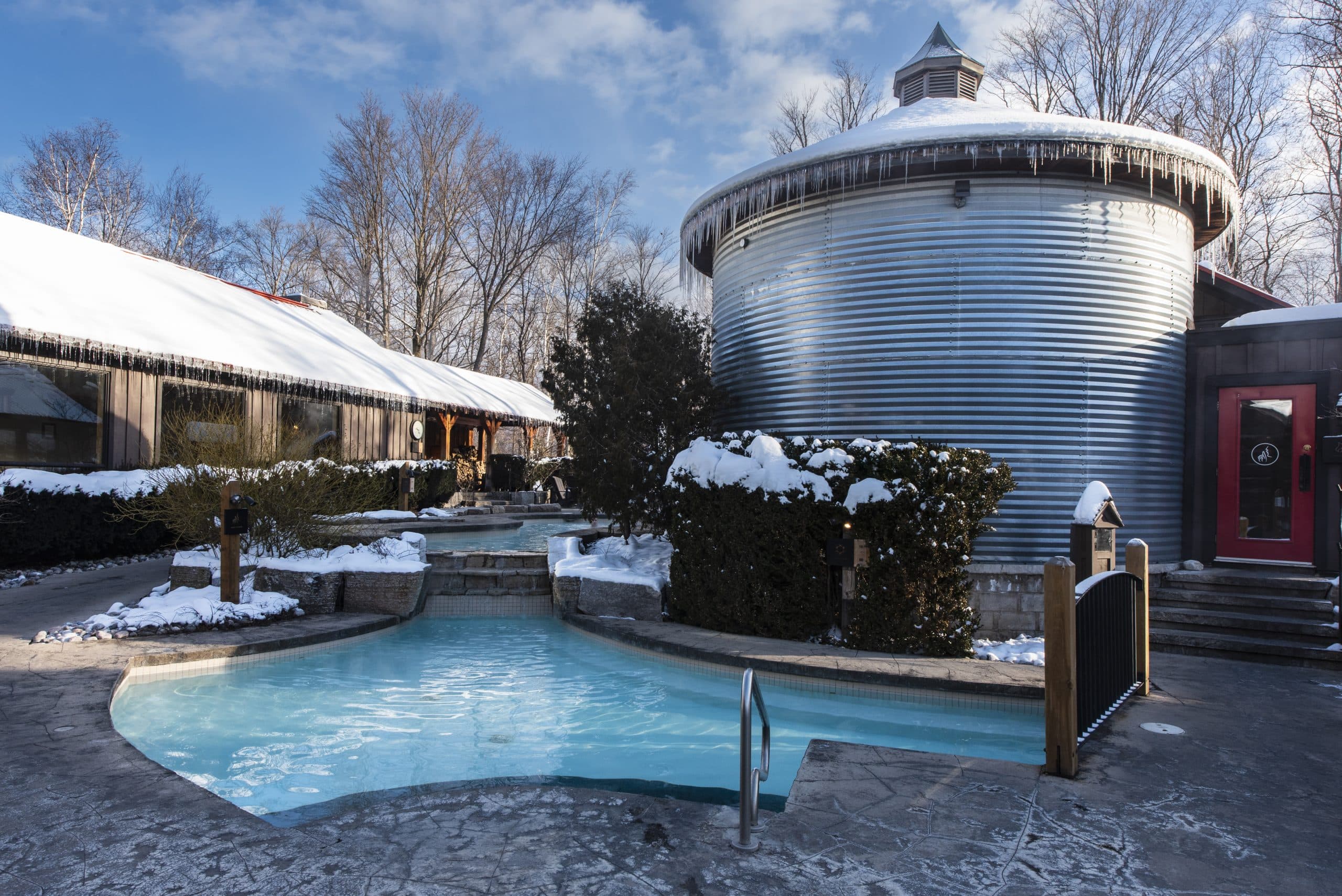 A serene winter scene featuring a heated pool surrounded by snow-covered trees and buildings.