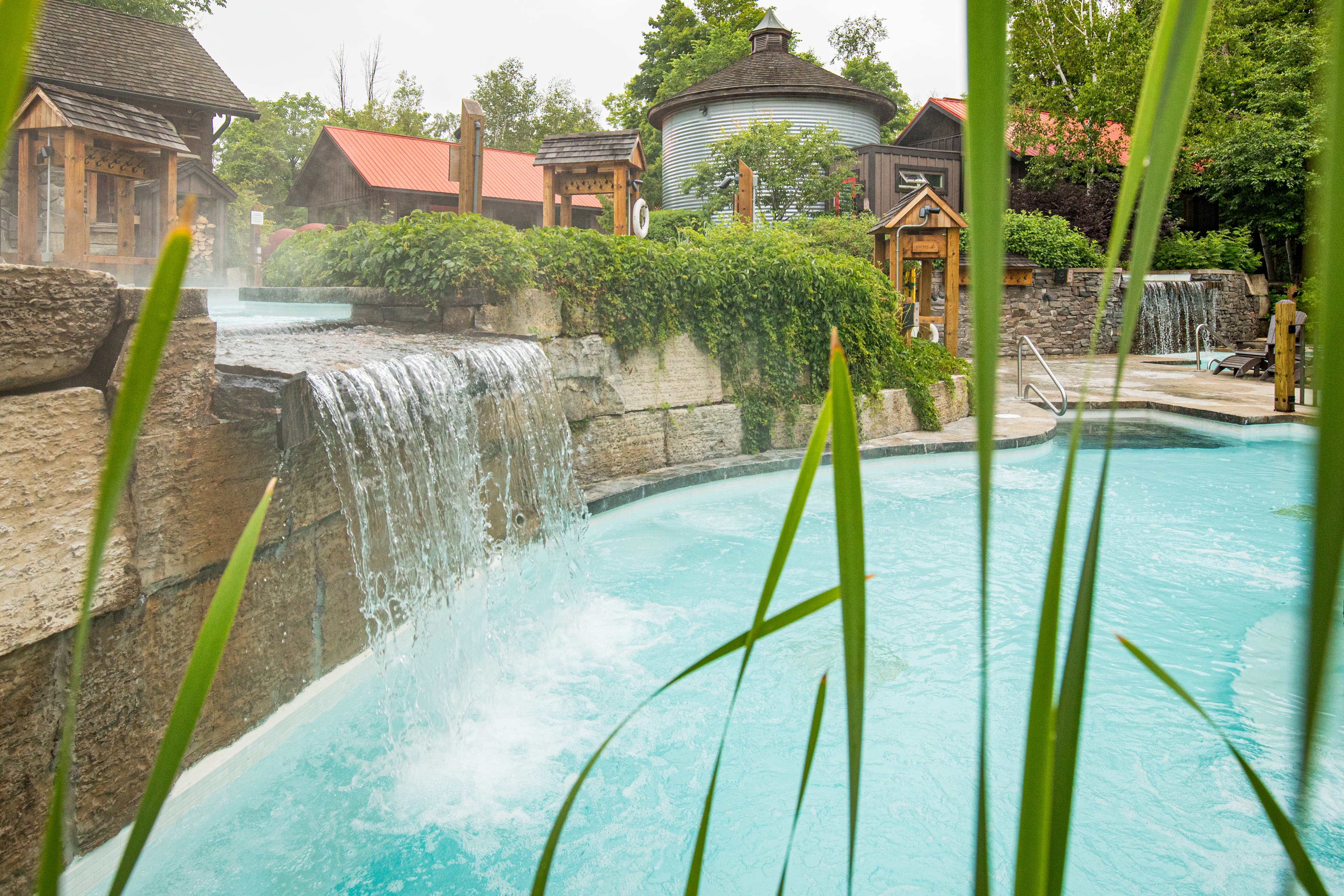 A peaceful pool area featuring a waterfall, stone structures, and lush greenery.