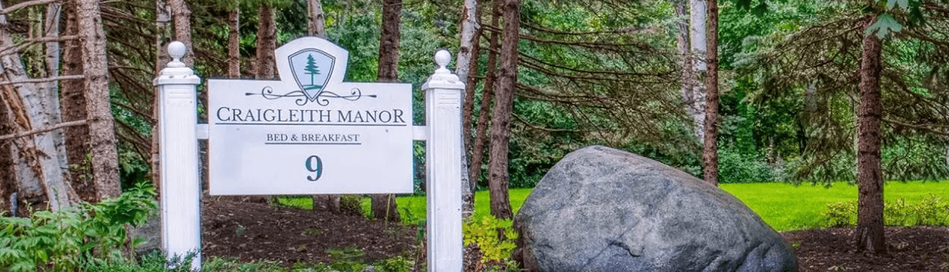Craigleith manor white monument sign with trees and large boulder in front of rock wall