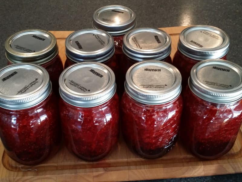 A collection of jars filled with red preserves arranged on a wooden cutting board.