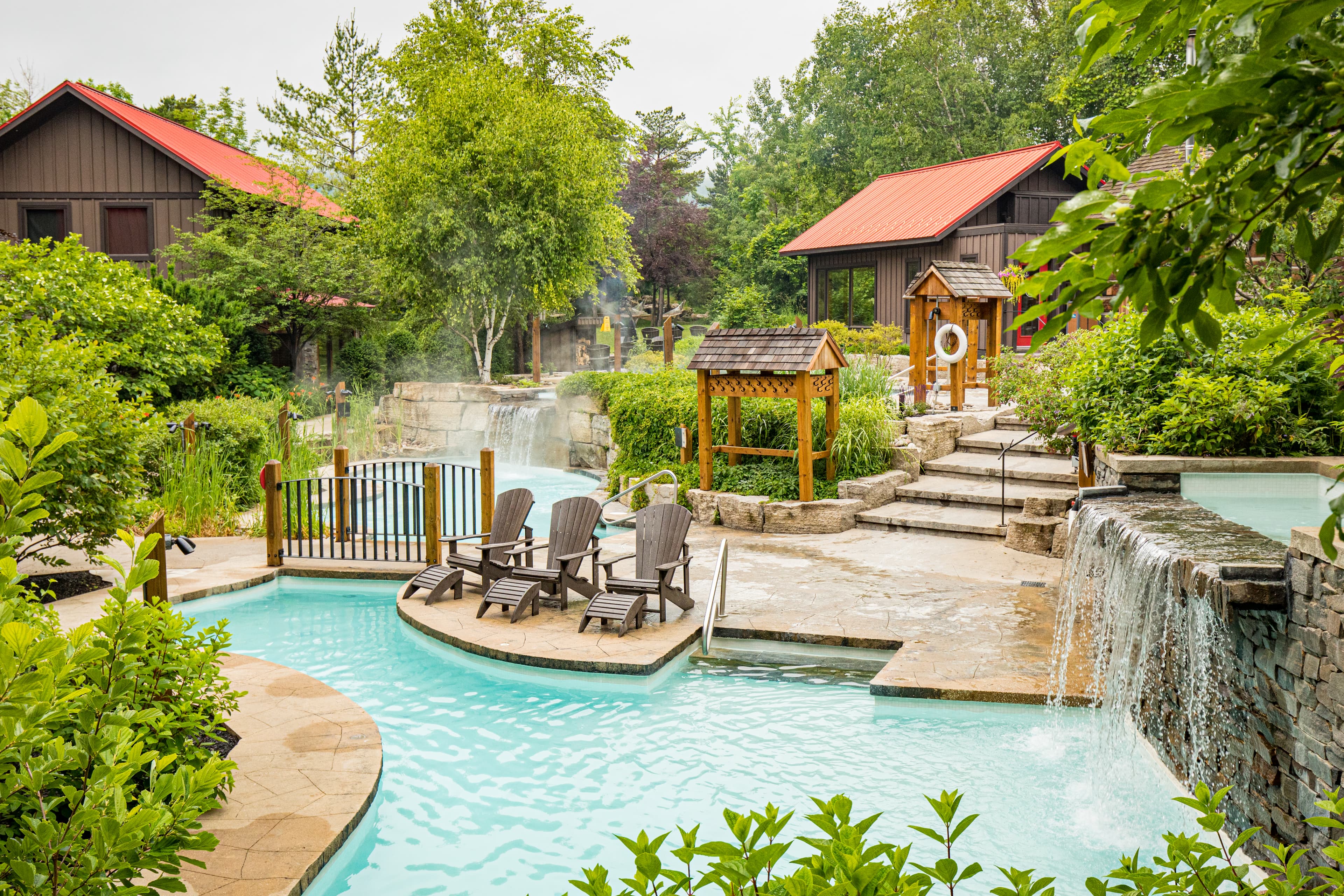 A serene outdoor pool area surrounded by lush greenery and rustic buildings.