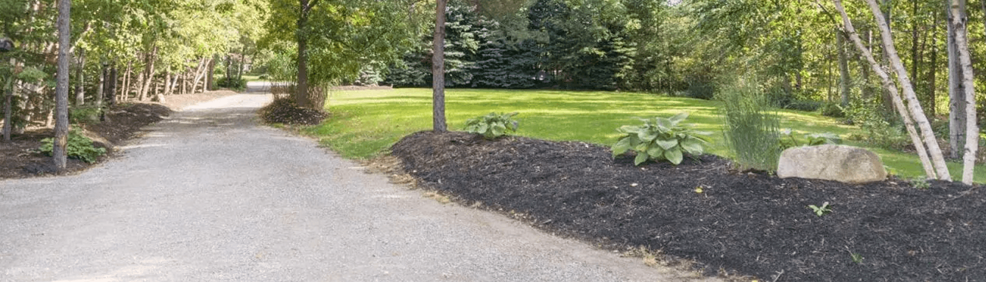 Winding driveway surrounded by trees, flower beds and green grass