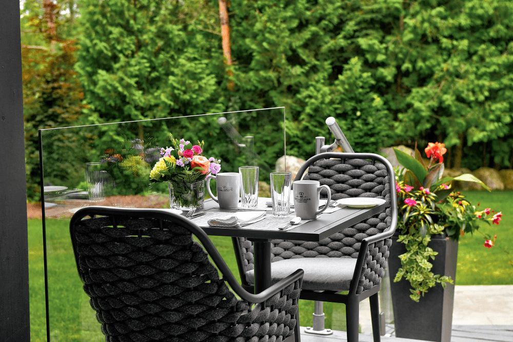 A stylish outdoor dining setup with a table, chairs, and floral arrangements surrounded by greenery.