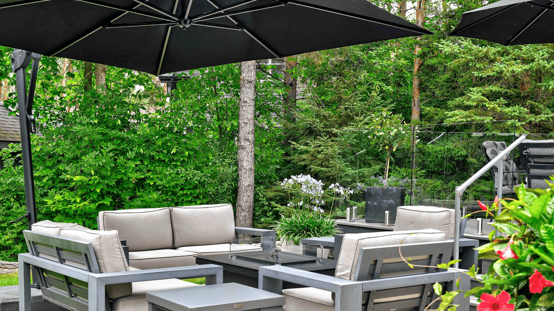 A cozy outdoor seating area with modern furniture and large black umbrellas surrounded by greenery.