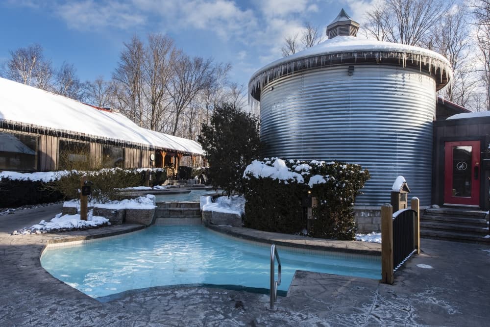 A winter scene featuring a circular building beside a small pool surrounded by snow-covered landscaping.
